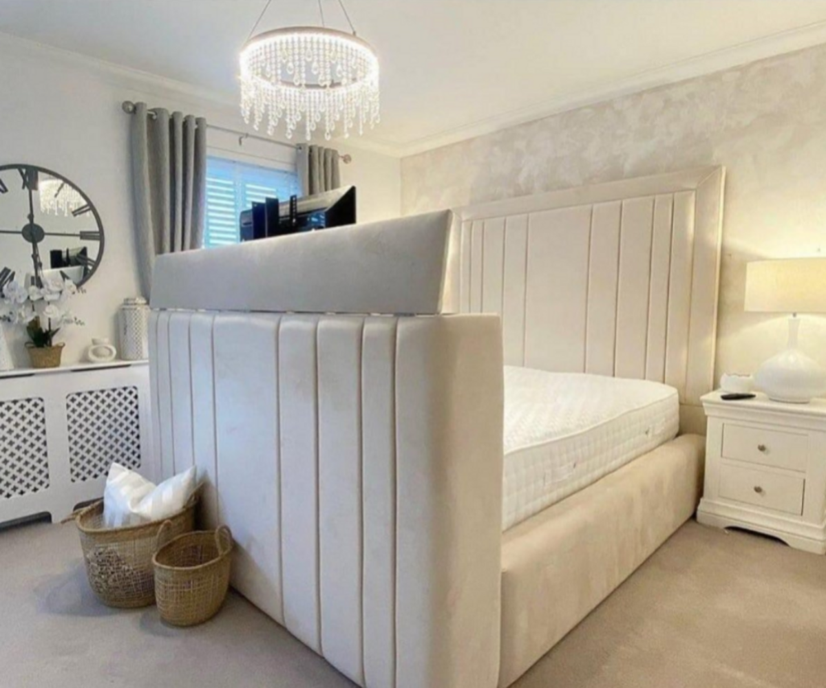 Beige divan bed with storage in a stylish bedroom featuring a chandelier, nightstand, mirror, and woven baskets.