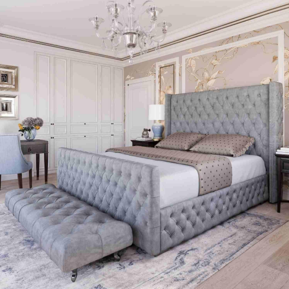 The bedroom showcases a sophisticated grey divan ottoman bed with a unique feature - a matching tufted bench that wheels smoothly underneath the footboard, creating a seamless and space-saving design while maintaining luxury and functionality.