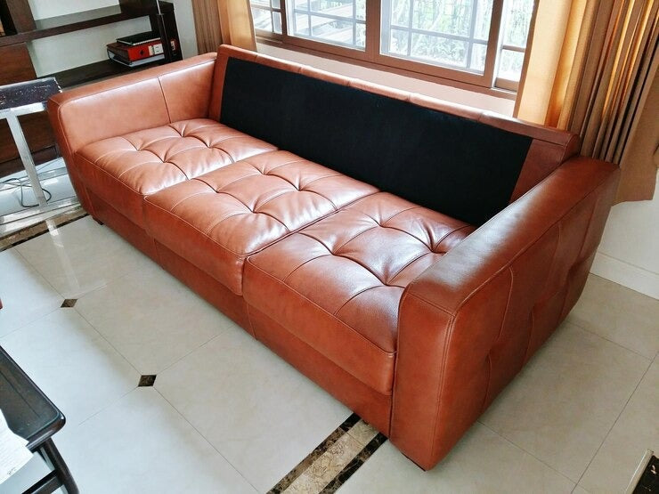 Leather sofa bed with tufted design and black fabric backrest in a well-lit room.