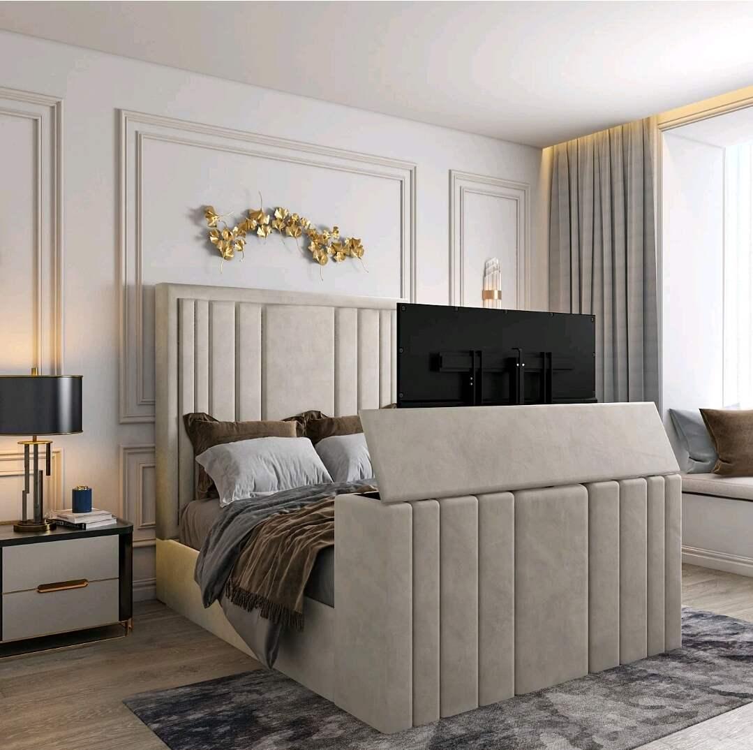 Modern bedroom with a cream-colored single Tv bed and mounted television, featuring gray and brown bedding, gold wall art, and a large window with gray drapes.