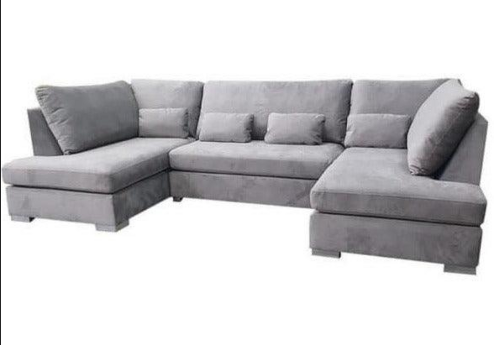 The large L-shaped sectional sofa from the Damascus Range features soft light gray upholstery and a contemporary design. It consists of three sections with plush boxy cushions, matching backrest cushions, and smaller throw pillows for added comfort, all resting on low block-style feet.