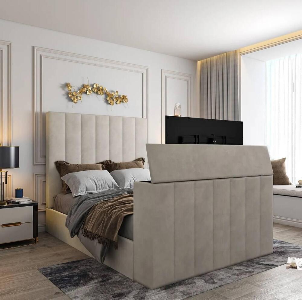 This modern bedroom features a Lynza TV bed with a tall light grey upholstered headboard and footboard. Styled with white and brown pillows, it includes a flat-screen TV at the footboard. A black lamp sits on the nightstand, and gold abstract wall art adds flair. Sheer curtains frame a large window, filling the room with light, while a cozy window seat and a grey patterned rug complete the look.