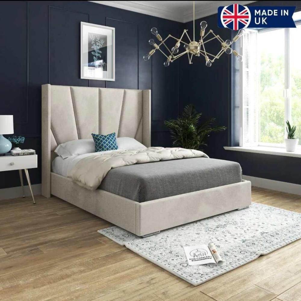 A modern bedroom with the Sunrise Wing Bed, featuring a cream-paneled headboard, white duvet, gray blanket, and blue pillow. Navy walls, light wood floors, and a chandelier add elegance. A white nightstand with a blue lamp and a large window complete the look.