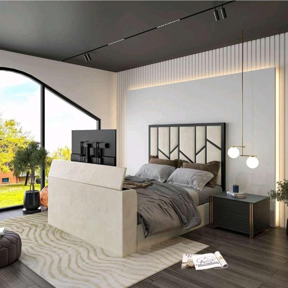 The image showcases a modern bedroom with a Zig Zag TV bed featuring a light-colored upholstered frame and a geometric black and cream headboard. The bedding includes shades of gray and dark throw pillows, with a pop-up TV in the footboard. A dark ceiling with minimal track lighting enhances the uniquely shaped window that lets in natural light. A beige and cream rug covers the dark wooden floor, complemented by a minimalist nightstand with a potted plant, a candle, and a hanging lamp. 